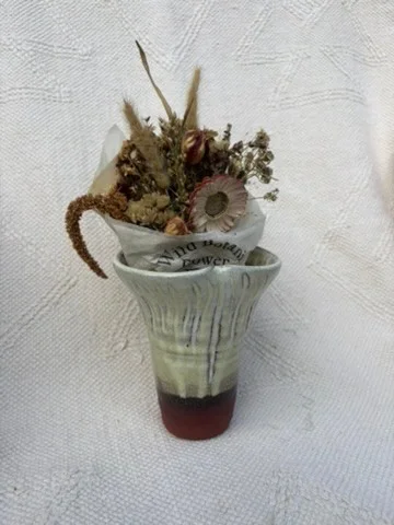 Green flared vessel holding dried flowers on a light gallery surface.