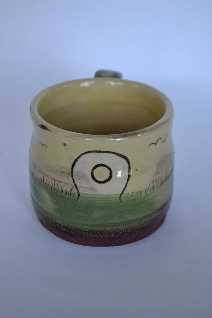 Green Mên an Tol mug with dark stone motifs and small birds.