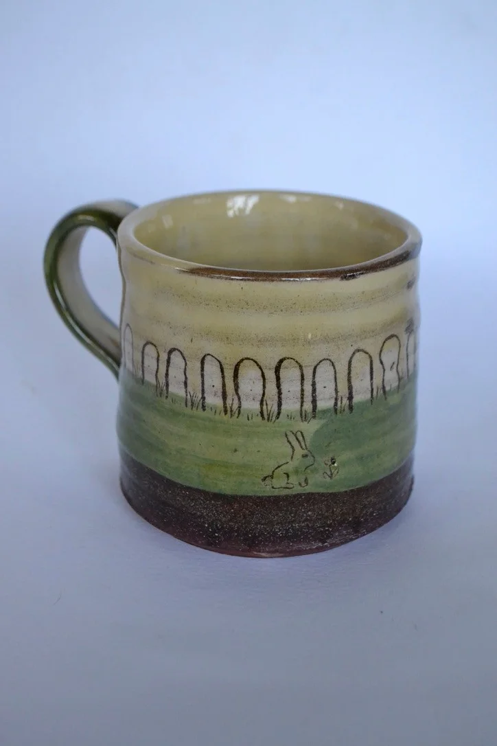 Green mug with dark standing stones, small birds and an earthy brown base.