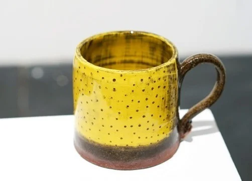 Yellow lemon mug with a rounded brown handle and earthy base on a light surface.