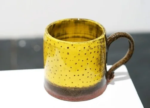 Yellow lemon mug with a rounded brown handle and earthy base on a light surface.