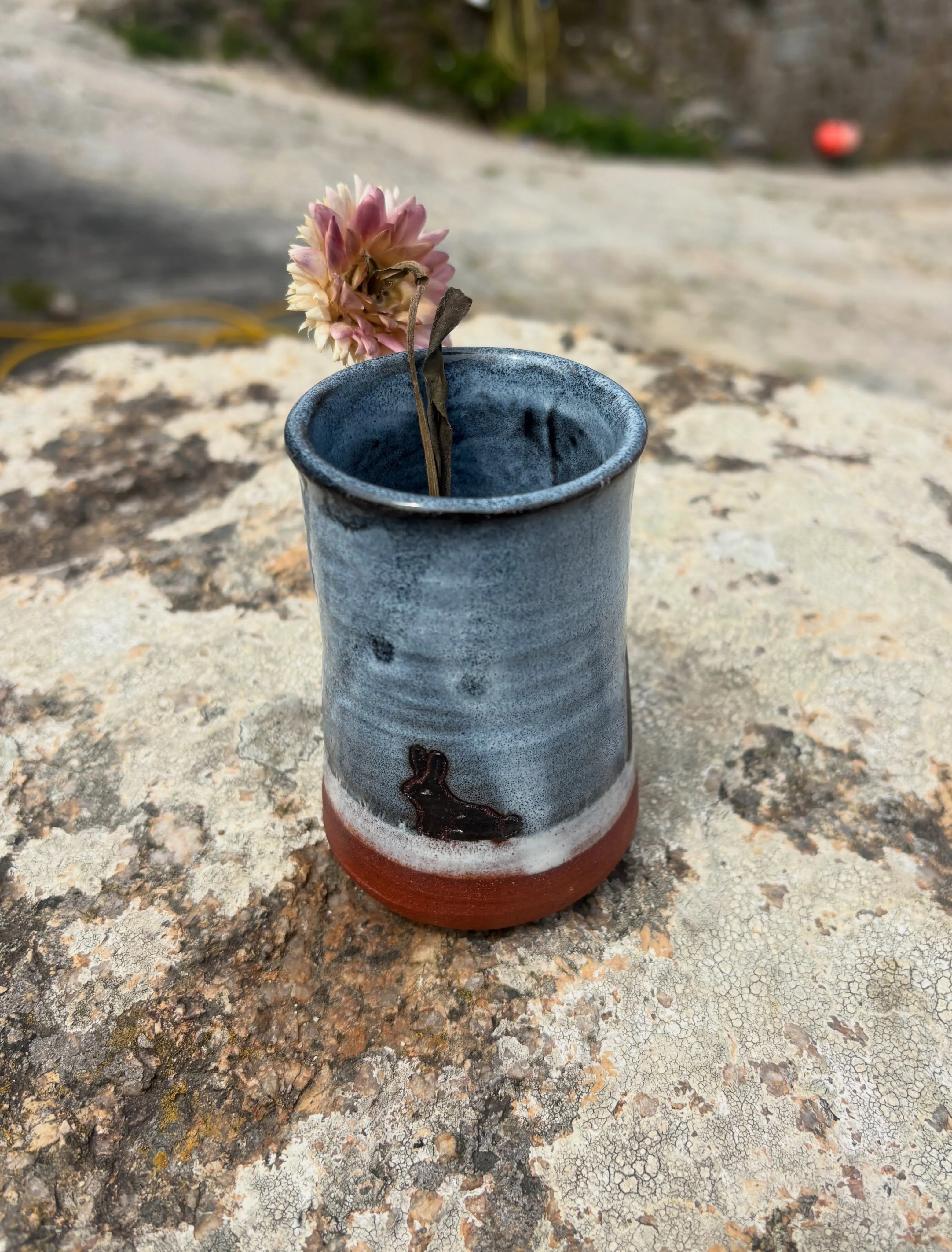 The reverse of the blue-grey bud vase, with a small dark rabbit above the terracotta-coloured base.