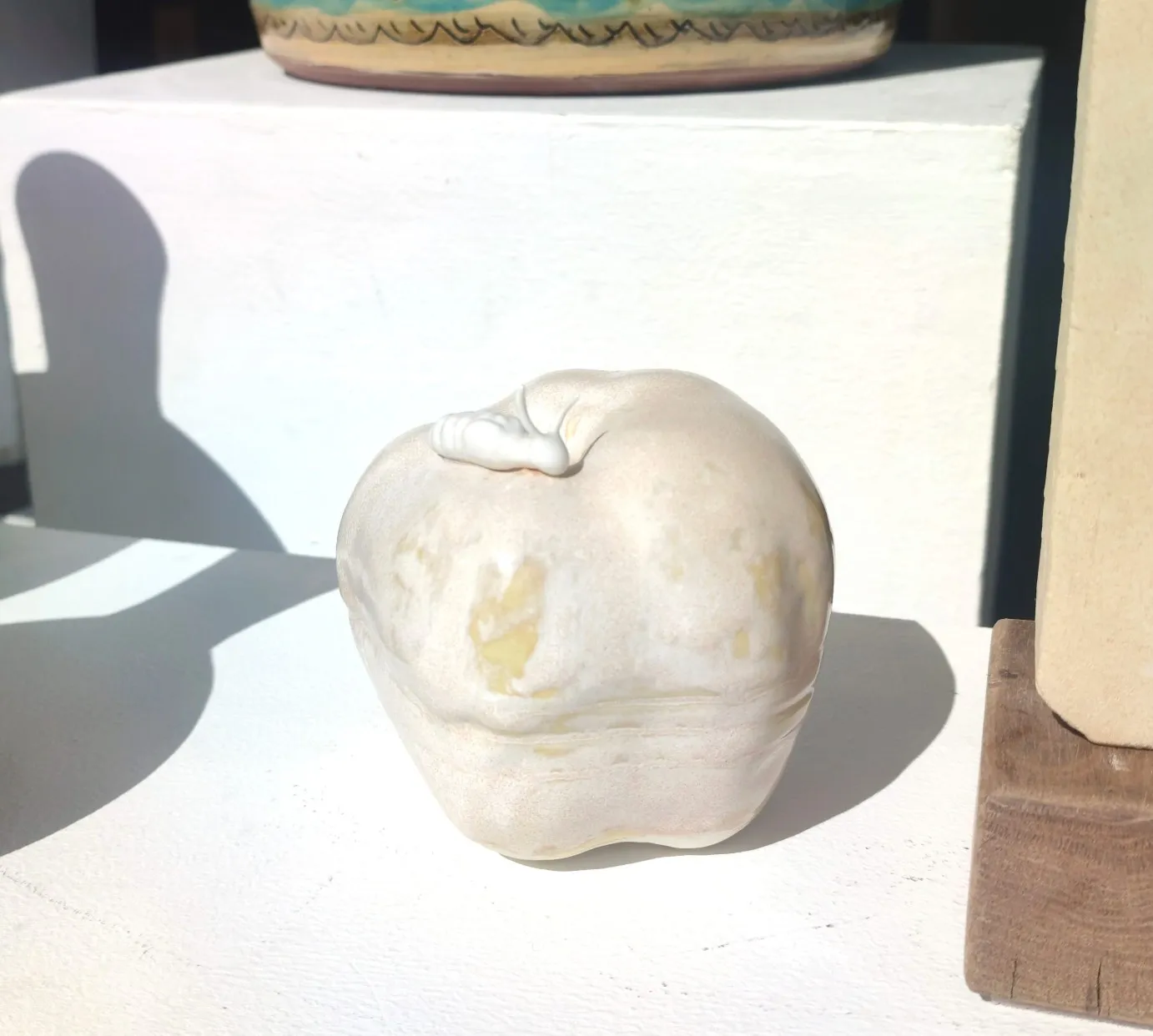 Pale porcelain apple with a small white insect on top.