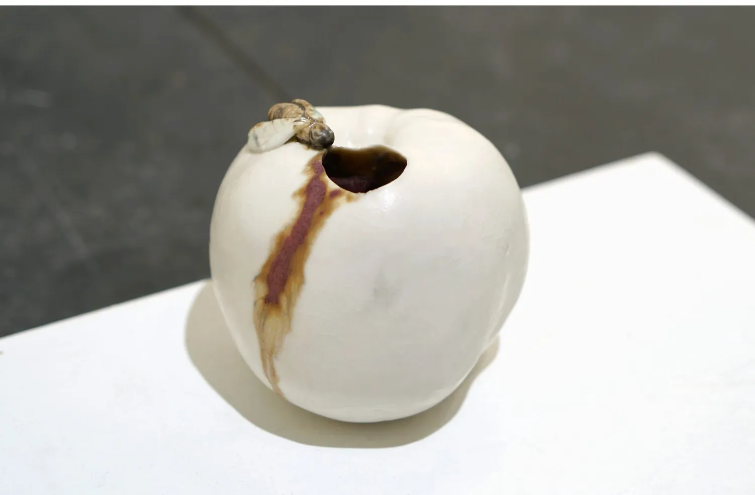 White porcelain apple with an opening and a dark glaze trail.