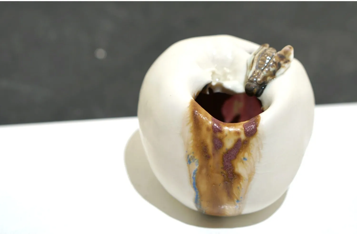 White porcelain apple with brown glaze flowing from its opening.