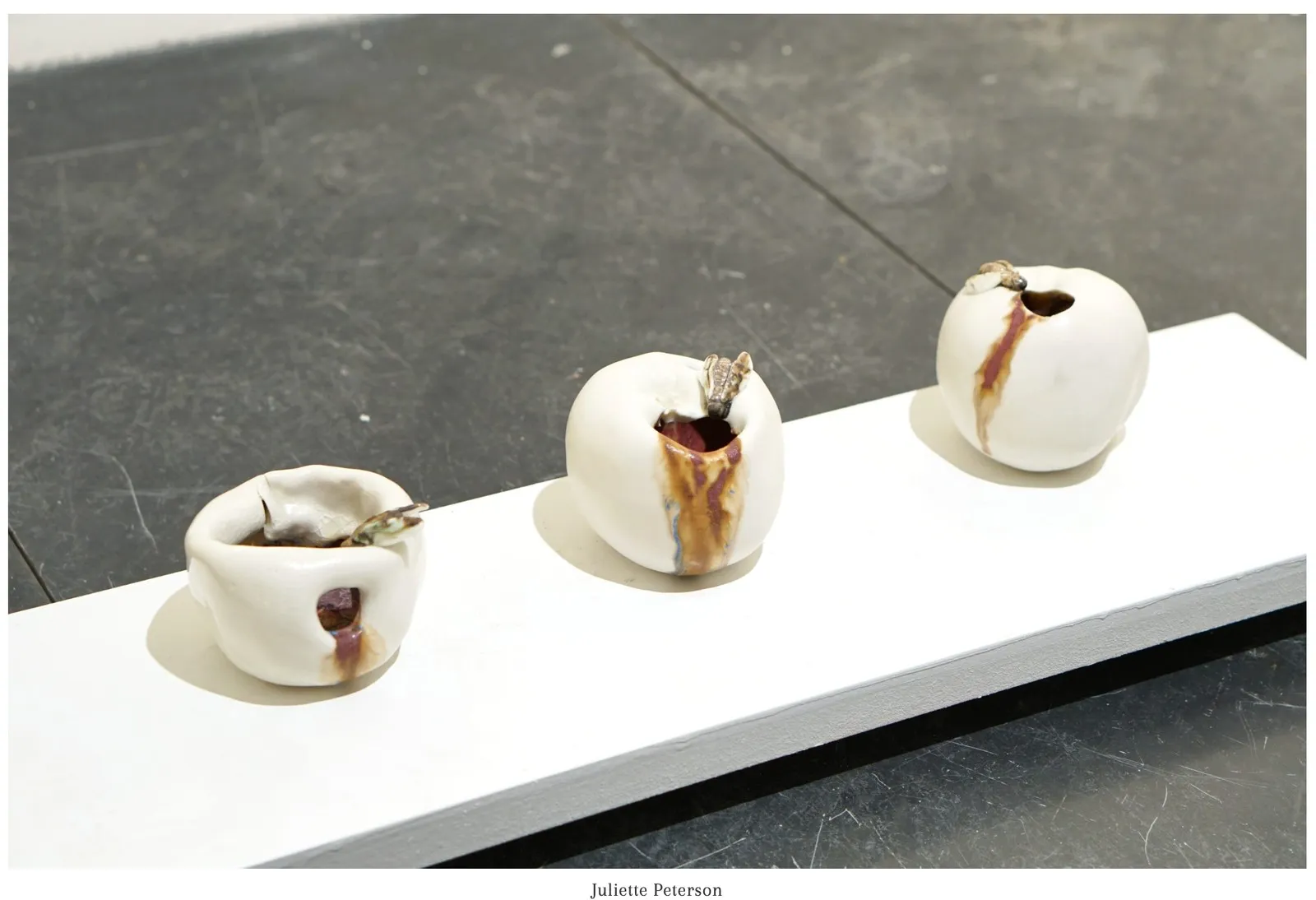 Three porcelain apple forms together on a long white plinth.