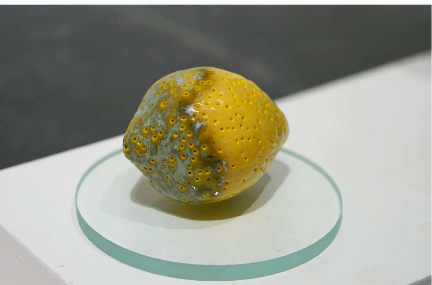A textured yellow porcelain lemon on a glass plate.