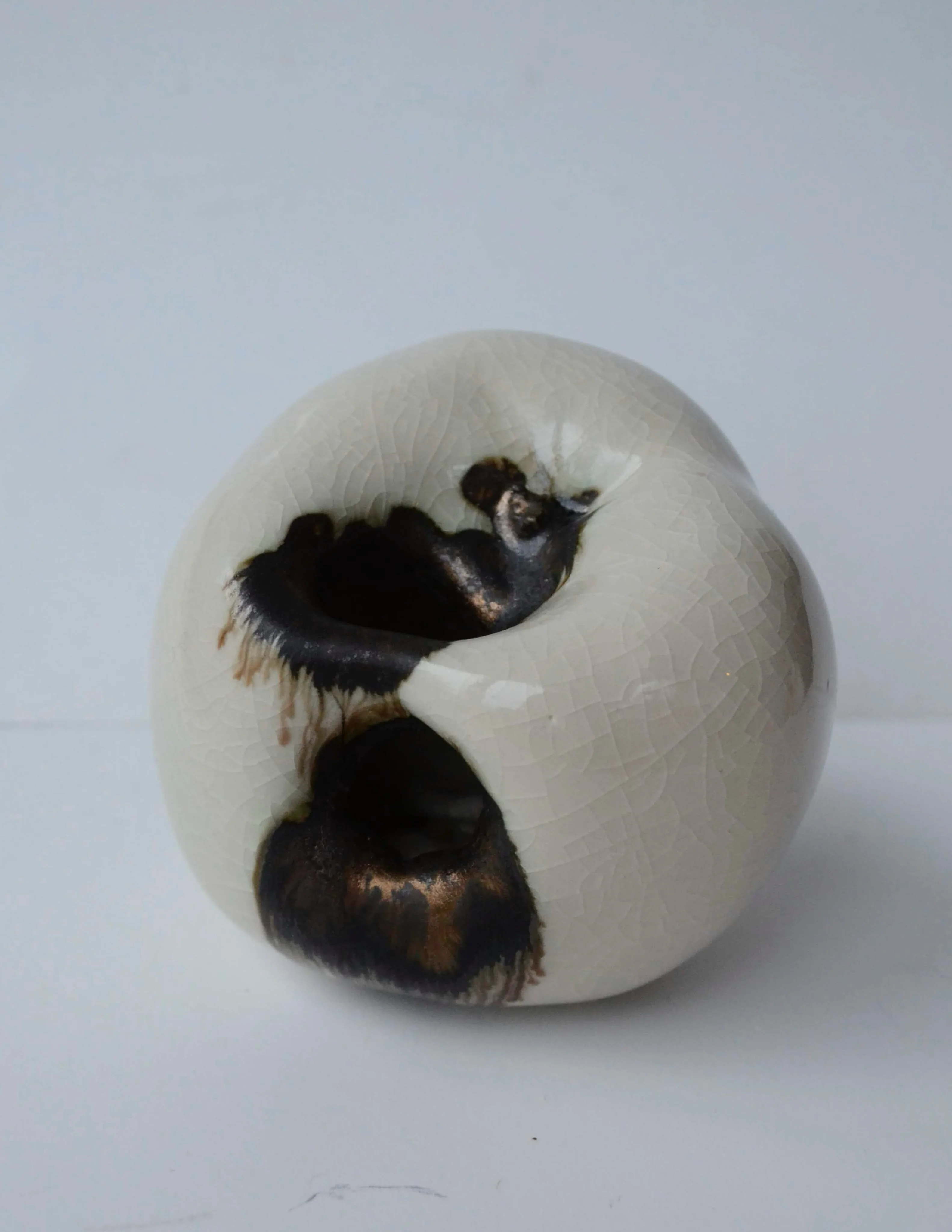 A pale porcelain apple sculpture with dark, broken-away areas exploring the appearance of decay.
