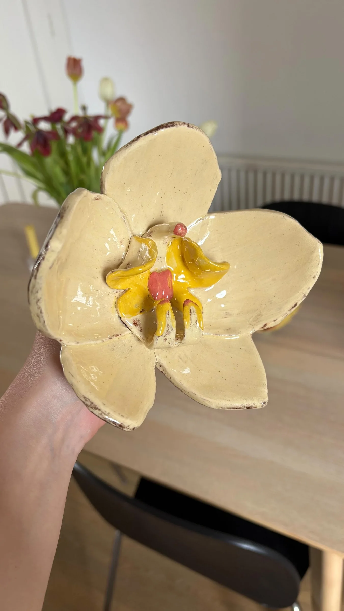 A hand holds a pale ceramic orchid with brown-edged petals, a yellow centre and small pink details.