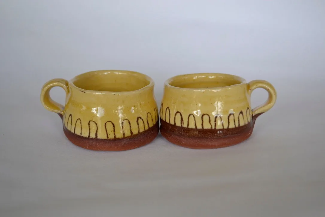 Two yellow mugs decorated with dark standing stones and flying birds.