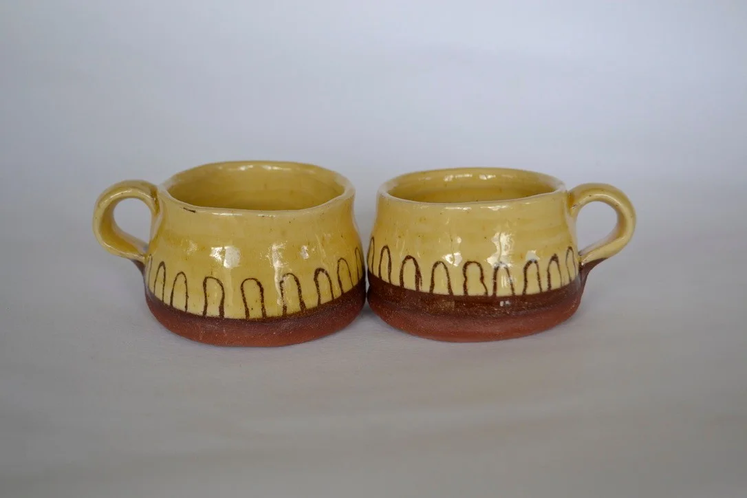 Two yellow mugs decorated with dark standing stones and flying birds.